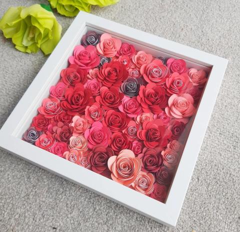 White picture frame containing various shades of salmon colored rolled flowers